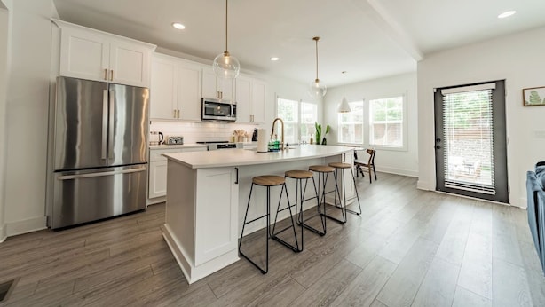 A modern kitchen with white cabinetry, stainless steel appliances, and a central island with bar stools. - Spacious Home-6 Beds | 10 Mins From City Center (Charlotte)