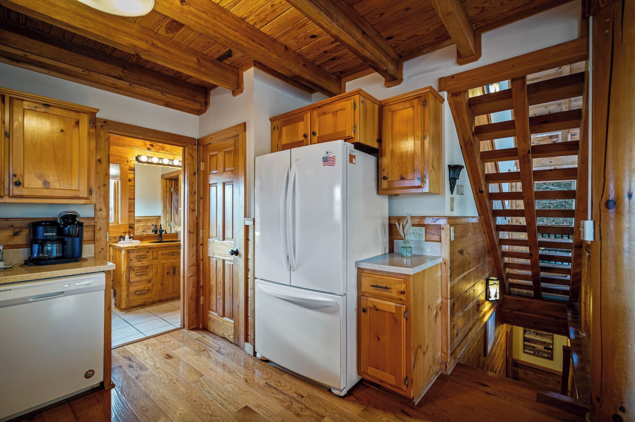 A kitchen with wooden cabinets, a white refrigerator, and a wooden staircase.