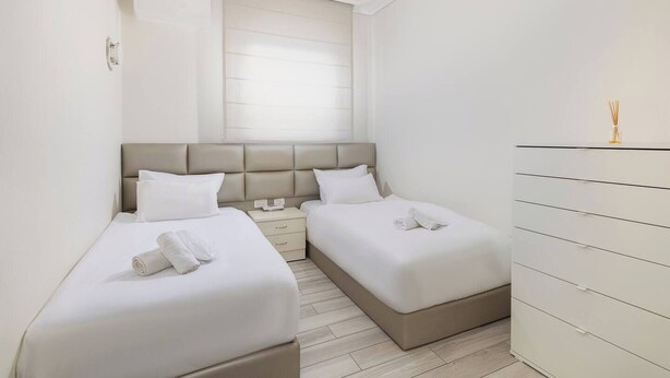 A hotel room with two beds, a dresser, a window with blinds, and a ceiling light. - 1 BR Apartment in Schneller Jerusalem Israel (Jerusalem)