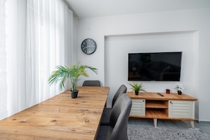 A modern conference room with a wooden table, two chairs, a potted plant, a clock, and a mounted TV. - Cozy Central Flat Near Marmaray in Uskudar (Istanbul)