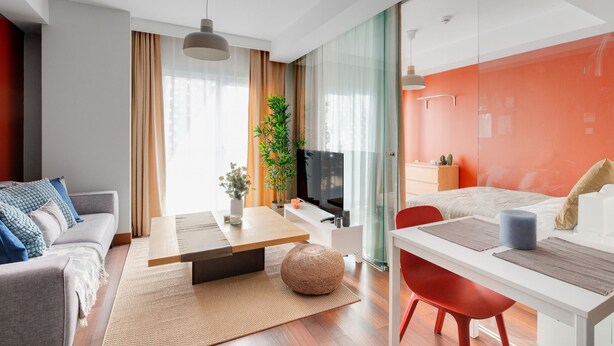 Un salon moderne avec un canapé, une table à manger et un téléviseur. Il y a une cloison en verre et un mur rouge.