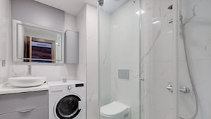 Une salle de bain moderne équipée d’un lave-linge intégré, de toilettes et d’une douche à parois de verre.