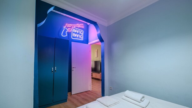 A hotel room with a neon sign reading "BANG BANG," a bed with neatly folded white towels, and a wooden floor. - Comfortable Home Steps from the Kadıköy Waterfront (Istanbul)