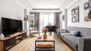 A modern living room with a flat-screen TV, a grey sofa, a wooden coffee table, and a dining area with a table and chairs. - Stylish New Apartment with Fast WiFi (Istanbul)