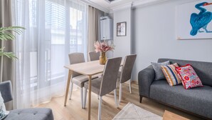Una sala de estar moderna con una mesa de comedor, un sofá gris y un ventanal con cortinas translúcidas.