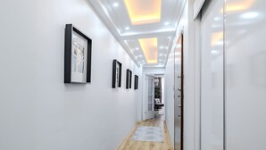 Un pasillo con cuadros enmarcados en las paredes, piso de madera y una puerta que da a otra habitación.