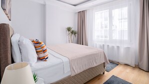 Un dormitorio ordenado con una cama, almohadas, una lámpara y una ventana con cortinas.