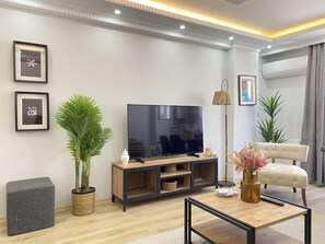 Ein modernes Wohnzimmer mit Flachbildfernseher, einer Couch, einem Couchtisch und Zimmerpflanzen.