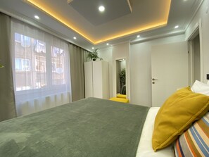Ein modernes Schlafzimmer mit einem großen Bett, einem begehbaren Kleiderschrank und Blick durch Vorhänge ins Freie.