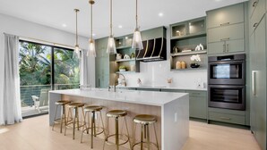 Een moderne keuken met een centraal eiland, barkrukken en een groot raam met uitzicht op een balkon.