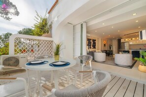 Een terras met een ronde tafel en stoelen, een potplant en een witte muur met een lattenwerkpatroon.