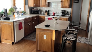 Een moderne keuken met houten kastjes, een centraal eiland en een eethoek met twee stoelen.