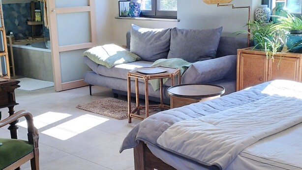 Una habitación con una cama, un sofá, una silla de madera, una mesita y una ventana.