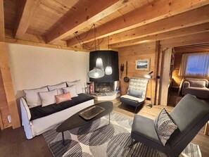 A cozy cabin interior with a sofa, armchair, and fireplace. - Family chalet in the Alps with a great view and 3 separate living areas. (Notre-Dame-de-Bellecombe)