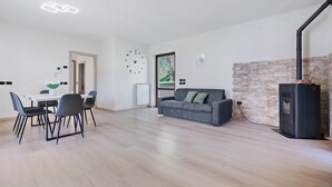 A modern living room with a dining area, a gray sofa, a fireplace, and a stone accent wall. - Casa L'Olivér Apartment Casaliva with Private Terrace and Lake View (Limone sul Garda)