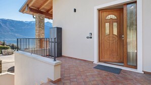 A wooden door with a glass panel, a stone pillar, and a metal railing on a balcony with a view of mountains. - Casa L'Olivér Apartment Casaliva with Private Terrace and Lake View (Limone sul Garda)