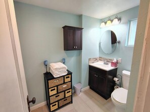 Ein Badezimmer mit hellblauer Wand, einem dunklen Holzschrank, einem weißen Waschbecken, einer Toilette und einer kleinen Mülltonne.