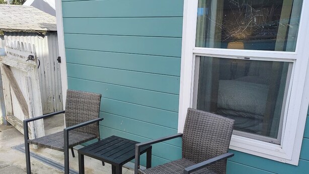 Eine Terrasse mit zwei Korbstühlen und einem kleinen Tisch, ein Fenster mit Ausblick und eine Gebäudeaußenfassade in Türkis.