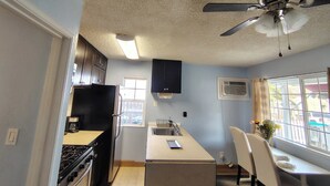 Eine kleine Küche mit Gasherd, Kühlschrank und Deckenventilator.