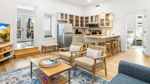 A modern kitchen with white cabinets, a refrigerator, and a microwave. There are wooden chairs and a blue sofa in the living area. - Fully Updated 2 Bedroom Apartment in Downtown - Just Steps Away from Green Lake (Green Lake)