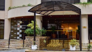 Entrada de hotel com área de estar coberta ao ar livre, degraus de pedra e plantas em vasos.