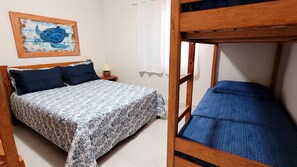 A room with a bed, a nightstand, a lamp, a painting, and a bunk bed. - Casa com churrasq a 750m da Praia de Juquehy/SP (São Sebastião)