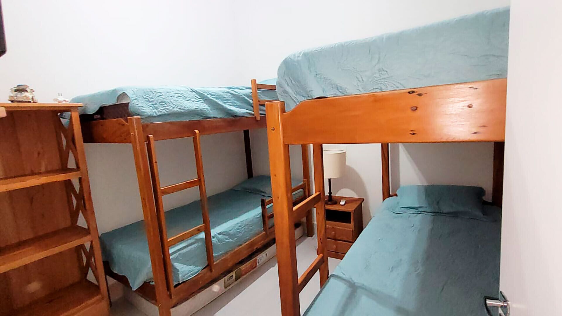 Een slaapkamer met een stapelbed, een houten ladder, een klein nachtkastje en een wandplank.