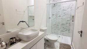 A modern bathroom with a large mirror, a white sink, a toilet, and a glass shower enclosure. - Casa com churrasq a 750m da Praia de Juquehy/SP (São Sebastião)