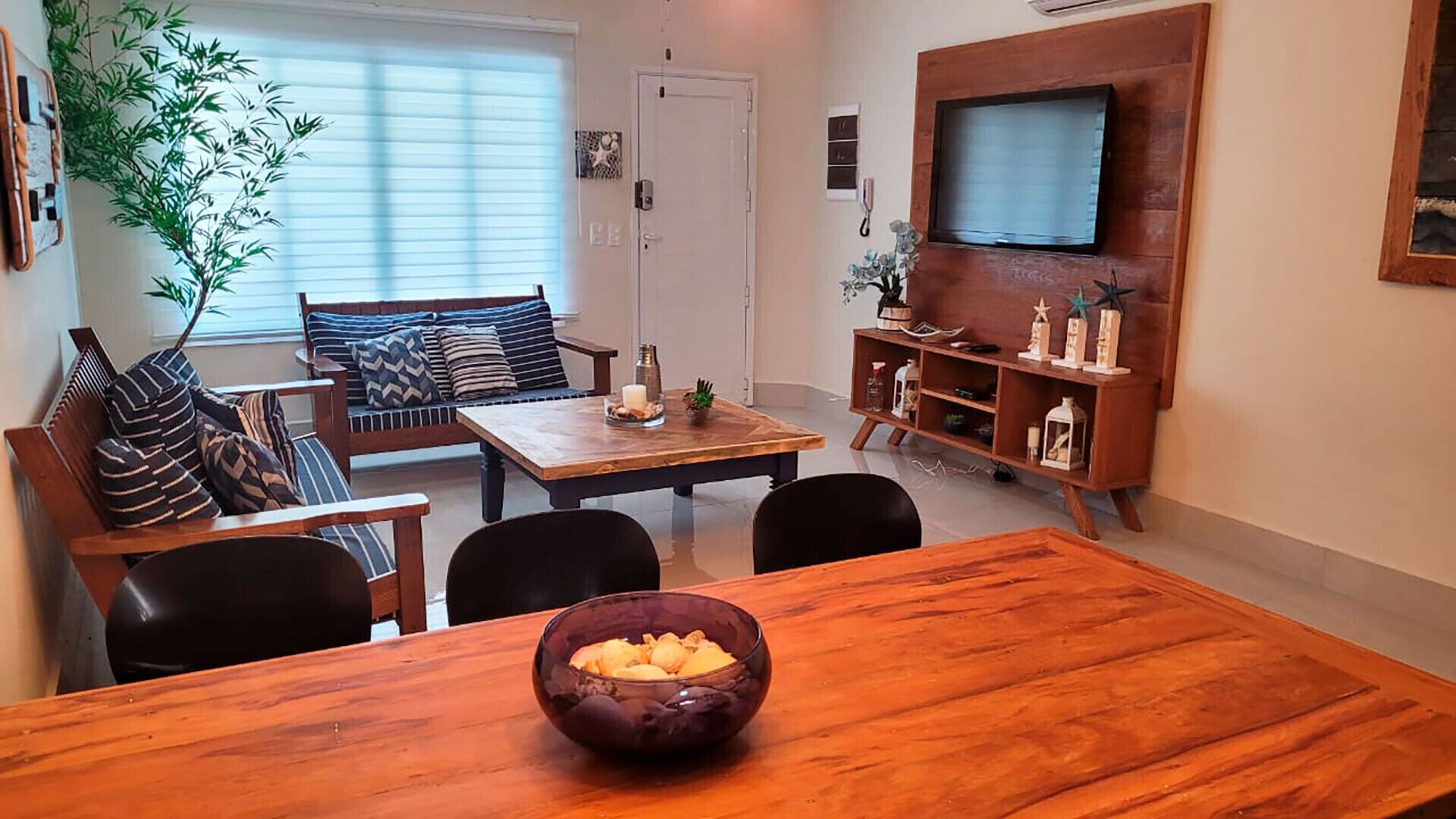 Ein Wohnzimmer mit einem Holzespeisetisch, einer Couch und einem an der Wand befestigten Fernseher.