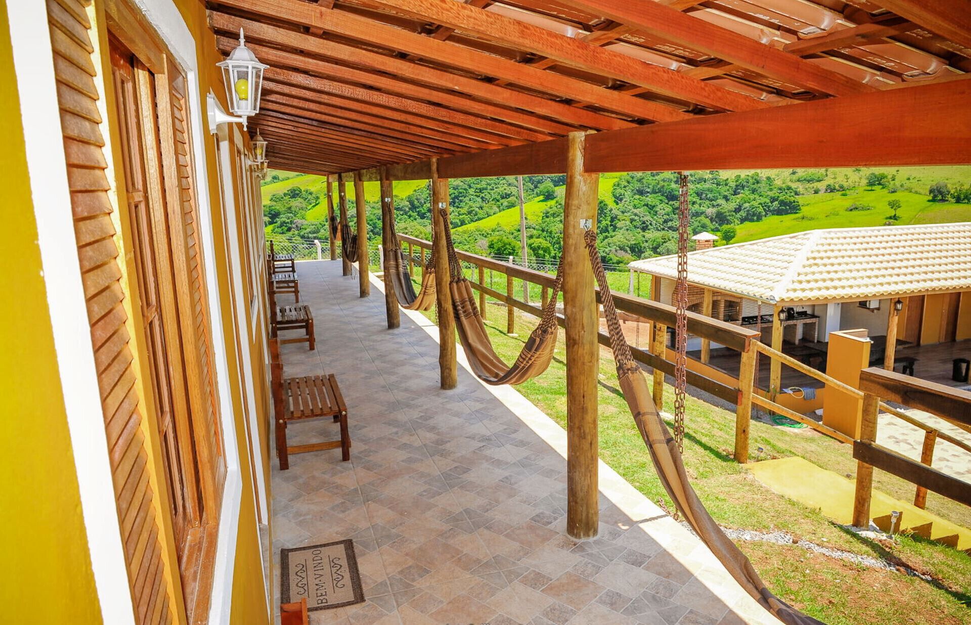 Un espacio al aire libre techado con bancos de madera, una hamaca y vistas a un paisaje verde.