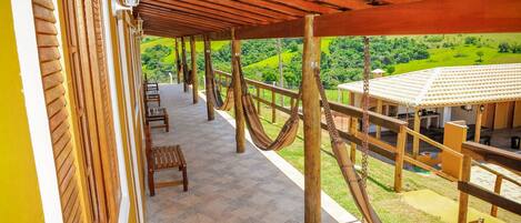 Un espacio al aire libre techado con bancos de madera, una hamaca y vistas a un paisaje verde.