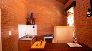A compact kitchen with a brick wall, a wooden countertop, a sink, a stove, and a refrigerator.