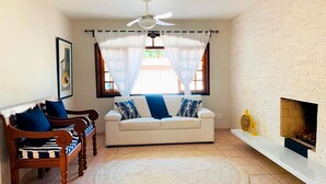 A living room with a white sofa, a wooden bench, a woven rug, a ceiling fan, and a fireplace. - Incrível casa a 13 min a pé da Praia de Juquehy/SP (São Sebastião)