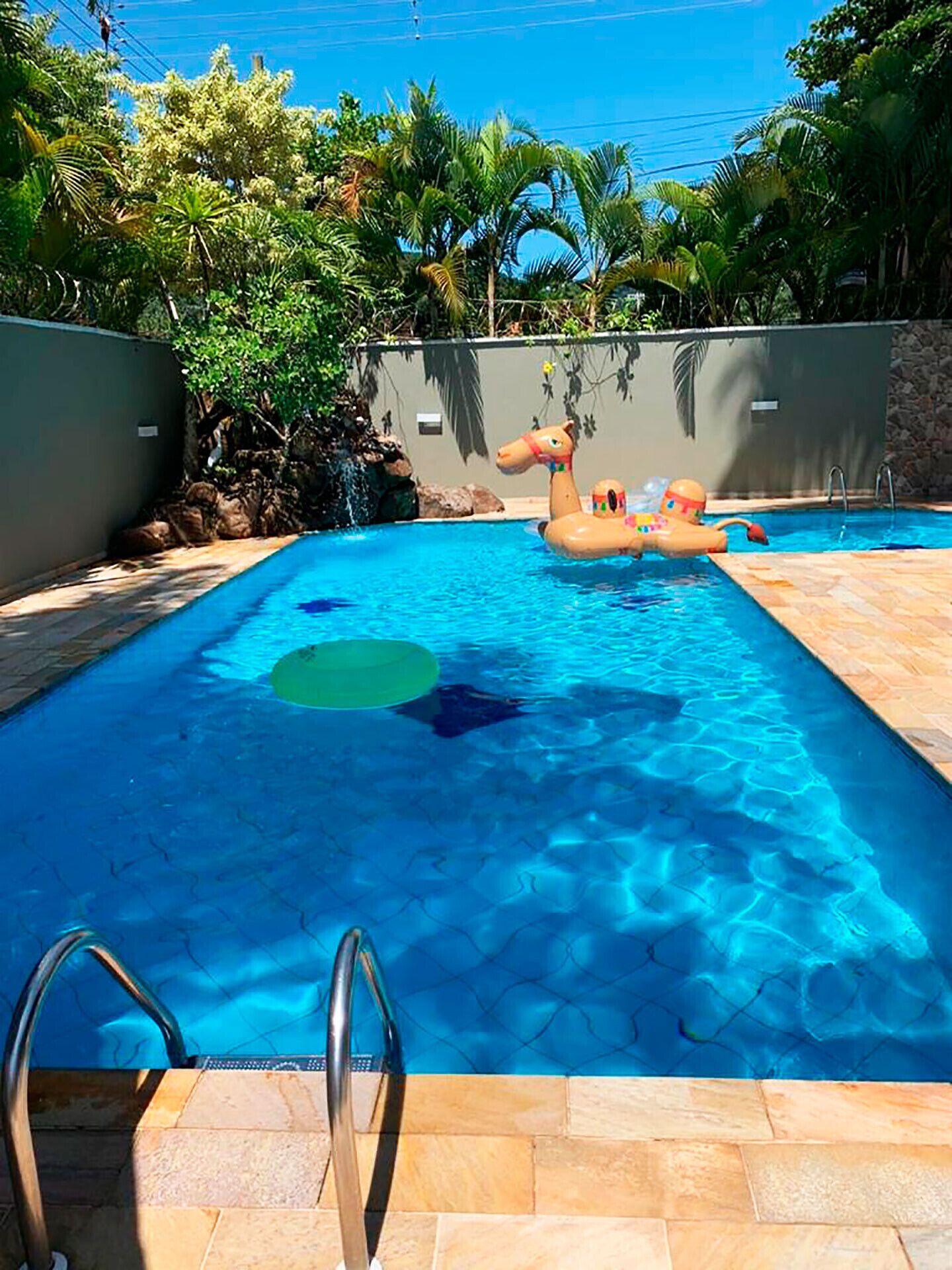 Une piscine à l’eau d’un bleu cristallin, entourée d’un mur de pierre et d’une végétation luxuriante.
