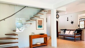 A modern interior with a glass staircase, a wooden console table, a black and white striped sofa, and nautical wall decor. - Incrível casa a 13 min a pé da Praia de Juquehy/SP (São Sebastião)