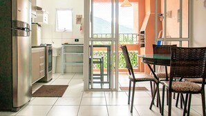 Una cucina con frigorifero, fornello e pensili, una zona pranzo con tavolo e sedie, e una porta scorrevole in vetro che dà su un balcone con vista.