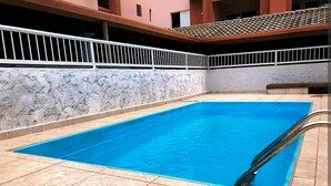 Una piscina rettangolare con bordo piastrellato, circondata da una ringhiera bianca e un muro in pietra.