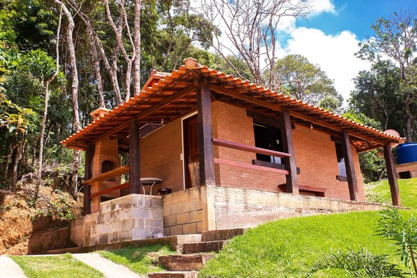 A rustic wooden cabin with a tiled roof, surrounded by lush greenery and trees.
