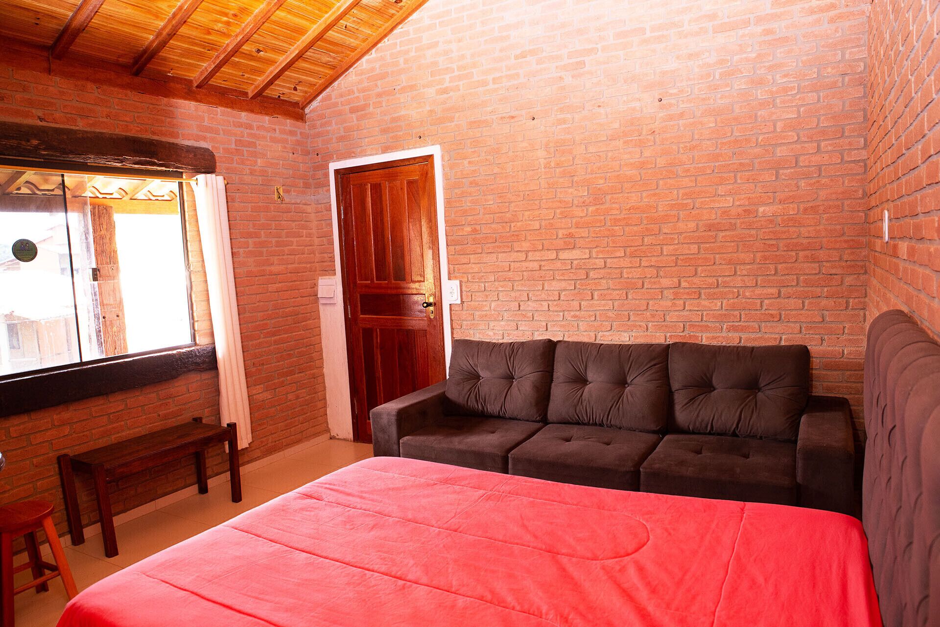 Ein Zimmer mit einer Ziegelwand, einer Holztür, einem braunen Sofa und einer roten Tagesdecke.
