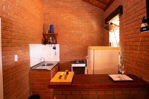 A compact kitchen with a brick wall, a wooden countertop, a sink, a stove, and a refrigerator.