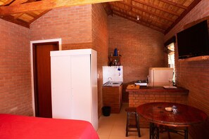A compact kitchen with a sink, a small refrigerator, and a wooden table with two stools. - Chalé para 3 com Rede e Churrasqueira | Ibitipoca (Conceição da Ibitipoca)