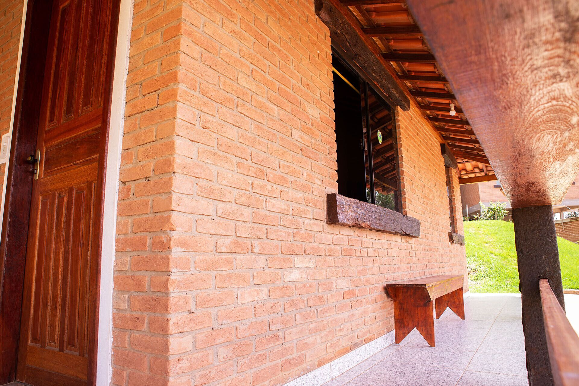 A brick building with a wooden door and window, a bench, and a covered outdoor area.