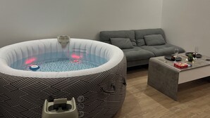 Un salon moderne avec un canapé gris, une table basse sur laquelle se trouvent un smartphone et une boîte, ainsi qu’un grand jacuzzi gonflable à la base bleue.