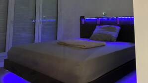 Une chambre à coucher avec un lit, une fenêtre avec des stores et un projecteur au plafond qui diffuse un motif coloré.