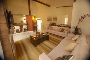Ein Wohnzimmer mit einer Couch, einem Couchtisch und einem Streifen Teppich. Im Hintergrund ist ein Essbereich mit Tisch und Stühlen zu sehen.
