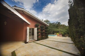 Ein Haus mit roter Fassade, einer weißen Tür und einer Steinterrasse, die zu einem Schwimmbad führt.