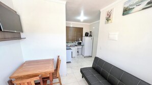 A compact living space with a dining table and chairs, a sofa, a kitchen area with appliances, and a painting on the wall. - Apto c Churrasqueira próx do Centro- Campo Grande (Campo Grande)