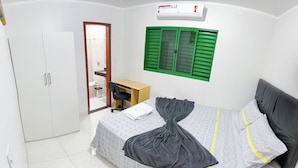 A bedroom with a bed, a desk, a wardrobe, and a bathroom visible through an open door. - Apto c Churrasqueira próx do Centro- Campo Grande (Campo Grande)