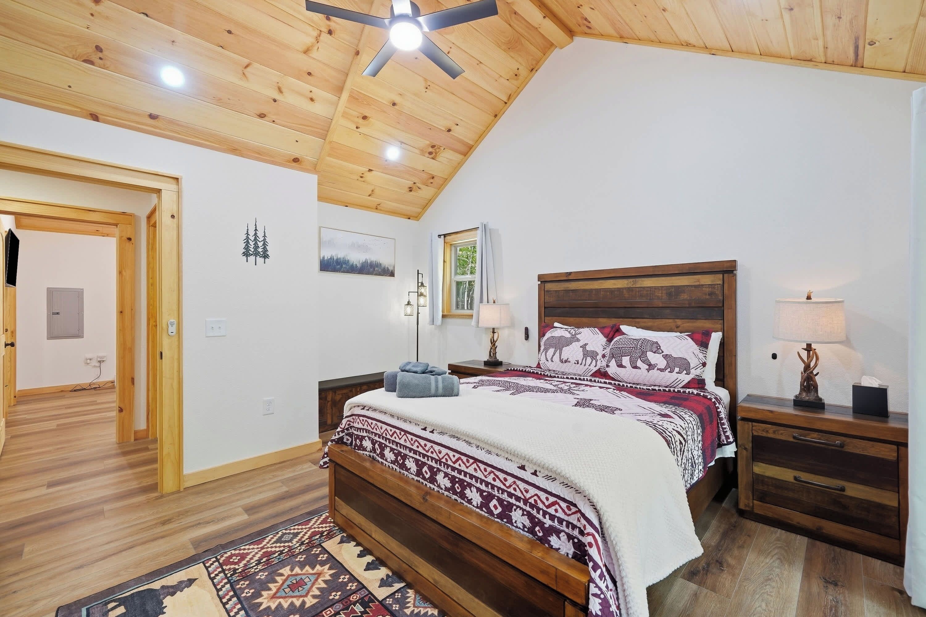 A bedroom with a wooden ceiling, a bed with patterned bedding, a nightstand with a lamp, and a rug on the floor.