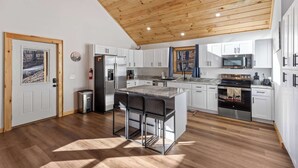 A modern kitchen with wooden ceiling, white cabinets, stainless steel appliances, and a bar area. - Embers Place - Murphy (Murphy)